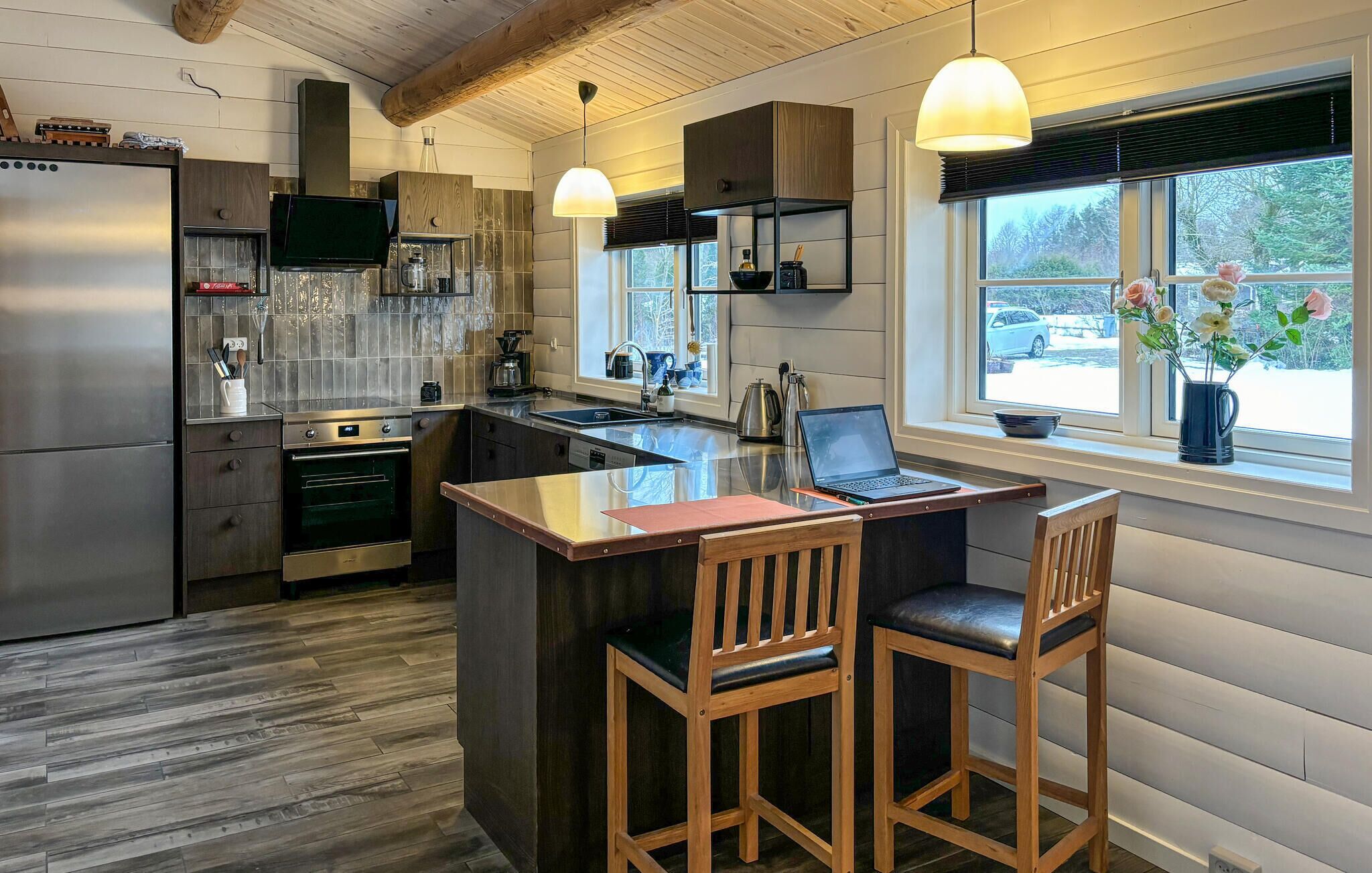 A modern kitchen with a central island, wooden chairs, and a laptop.