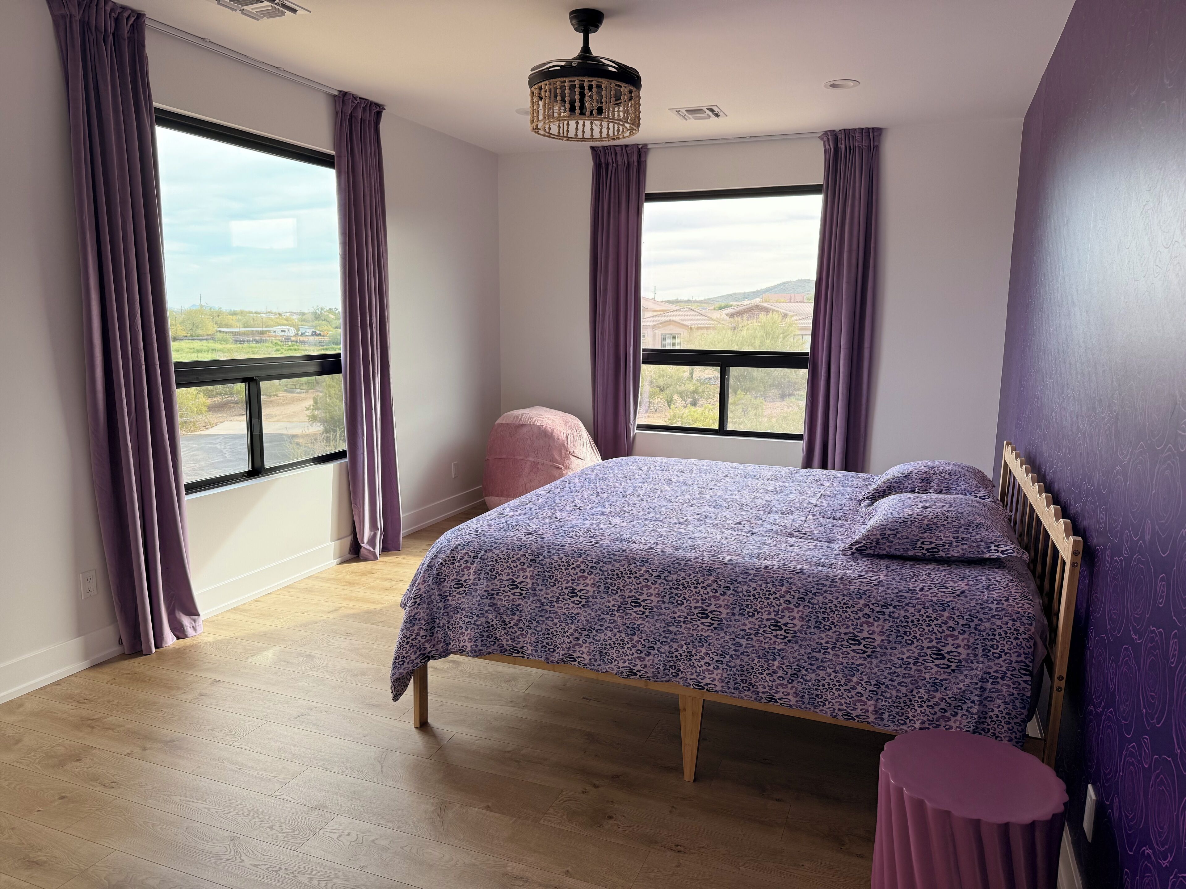 A bedroom with a large bed, wooden floor, and a view of the outdoors through a window.