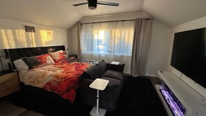 A modern bedroom with a bed, a small sofa, a TV, and a ceiling fan. - 85-in TV|Massage Sofa|3 KING Beds|Walk to UT: ½ mi (Austin)