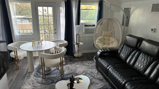 A modern living room with a black leather sofa, a round white table with chairs, a hanging chair, and a marble-patterned rug. - 85-in TV|Massage Sofa|3 KING Beds|Walk to UT: ½ mi (Austin)