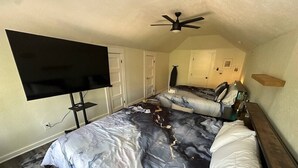 A bedroom with a bed, a TV on a stand, a ceiling fan, and a door. - 85-in TV|Massage Sofa|3 KING Beds|Walk to UT: ½ mi (Austin)