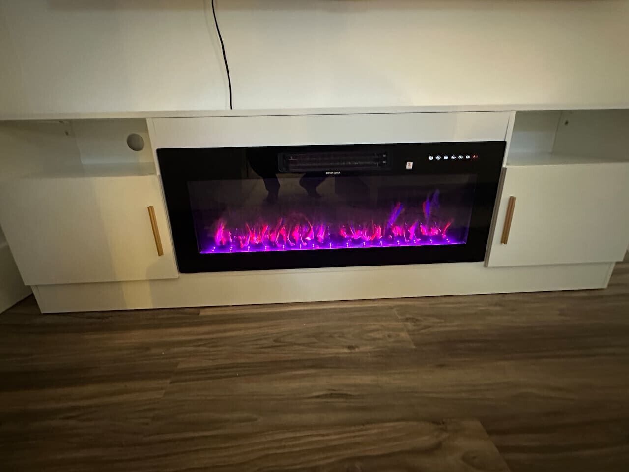 Moderni takka, jossa on digitaalinen näyttö, ja se on sijoitettu valkoiseen kaappiin, jonka alla on puulattia.