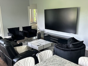 Una sala de estar moderna con un televisor de pantalla plana grande, sofás de cuero blanco y negro, una mesa de centro de mármol y un otoman negro.