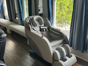Una silla de masaje con panel de control, ubicada cerca de una ventana con cortinas.