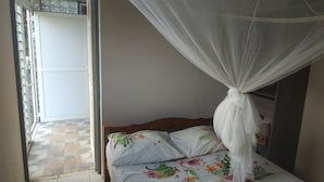 A bedroom with a bed, a mosquito net, and a view of the outside. - Appart close to everything. (Gros-Morne)