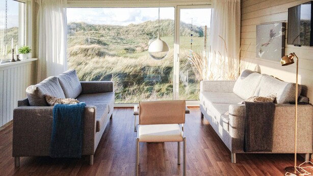 Een woonkamer met twee banken, een bijzettafeltje en uitzicht op een grasrijk landschap door grote ramen.
