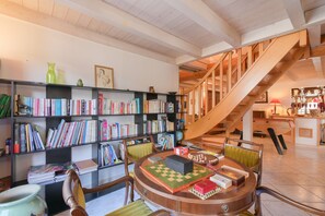 A spacious room with a wooden staircase, a round table with chess pieces, and bookshelves filled with books. - Accessible Apartment “La Padouck” with Mountain View, Private Terrace and Wi-Fi (Thônes)