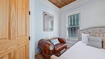 Un dormitorio con un sofá con forma de coche antiguo, una cama grande con colchón acolchado, techo de madera y una ventana con persianas.
