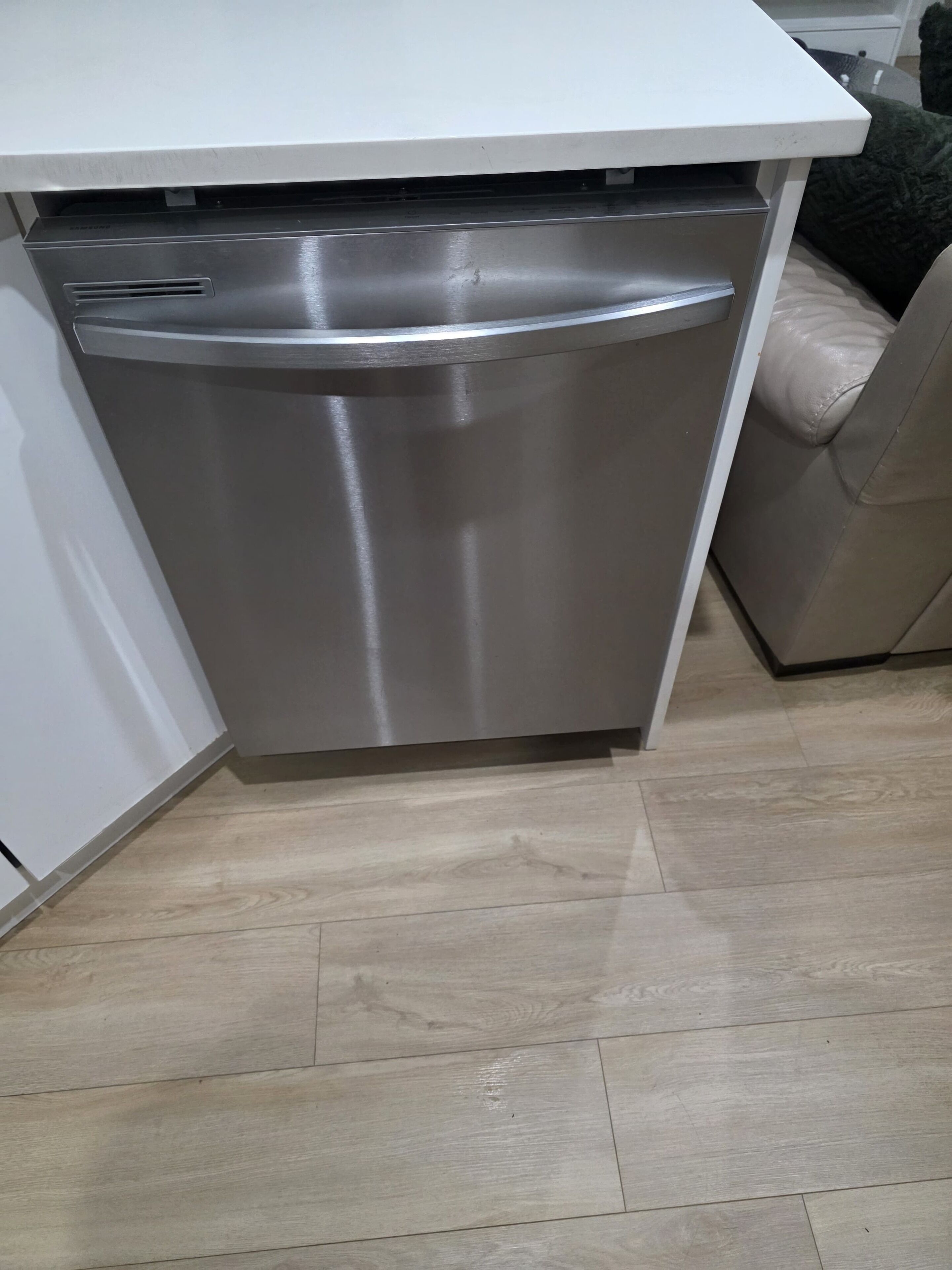 A compact kitchen with a built-in dishwasher, wooden flooring, and a white countertop.