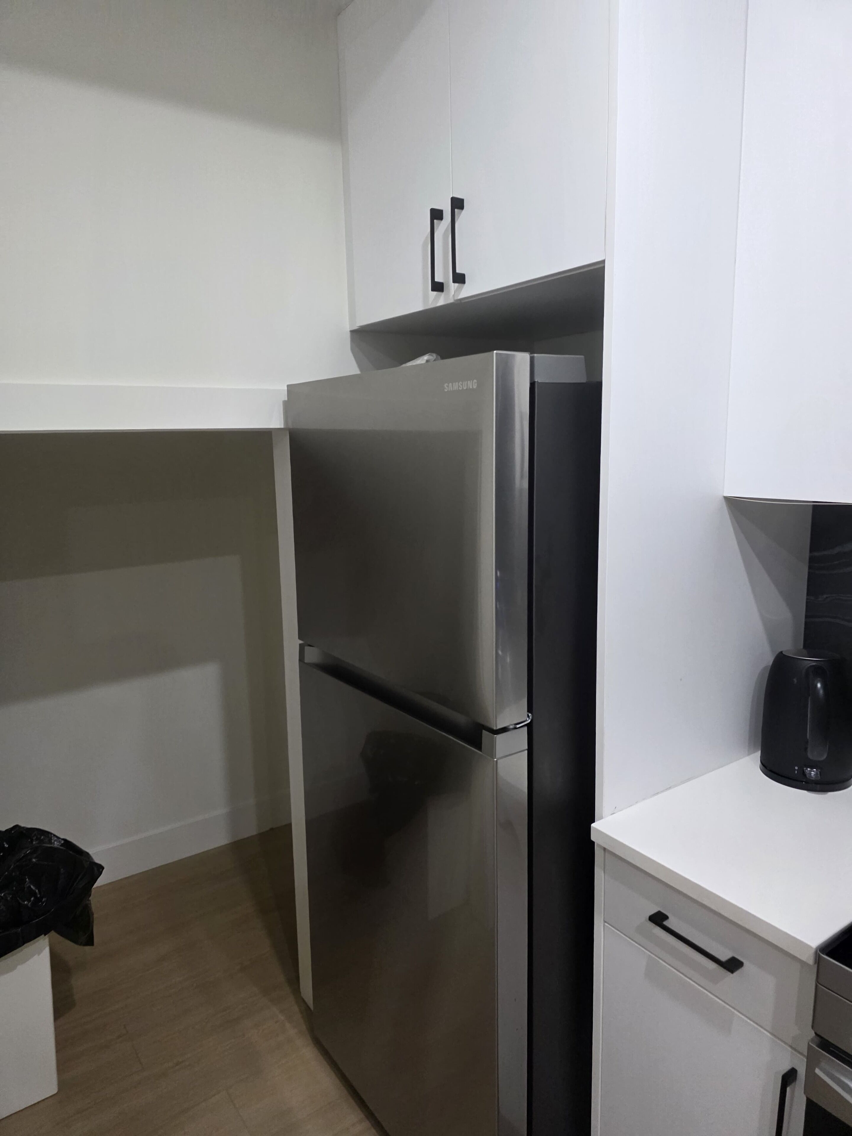 A compact kitchen with a stainless steel refrigerator, a white countertop, and a black coffee maker.