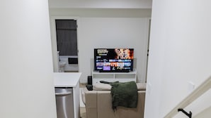 En smal hall leder in till ett vardagsrum med en soffa, en tv och ett köksutrymme.