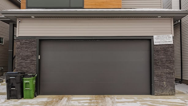 Ett modernt hus i två v åningar med ett garage, en accentvägg i sten och en klarblå himmel.
