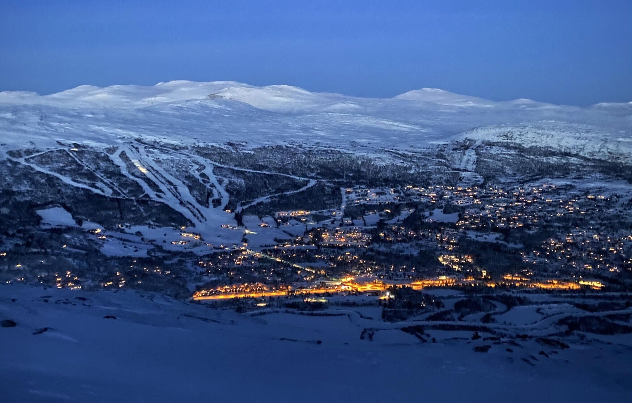 Paisatge de muntanyes nevades amb un poble il·luminat per llums.