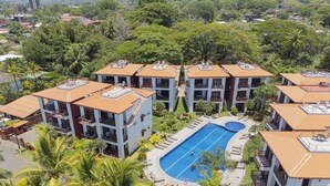 A resort with multiple buildings, a central swimming pool, and surrounding palm trees.