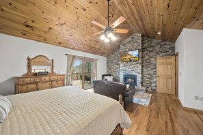 A bedroom with a large bed, wooden ceiling, a fireplace, a dresser, and a door leading to a balcony. - Blowing Rock Retreat - Hot Tub | Sleeps 10 | Mountain Views (Blowing Rock)