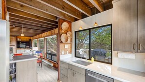 A modern kitchen with a large window, wooden ceiling beams, and a built-in dishwasher. - House 25 | 4 Bedroom (Watsonville)