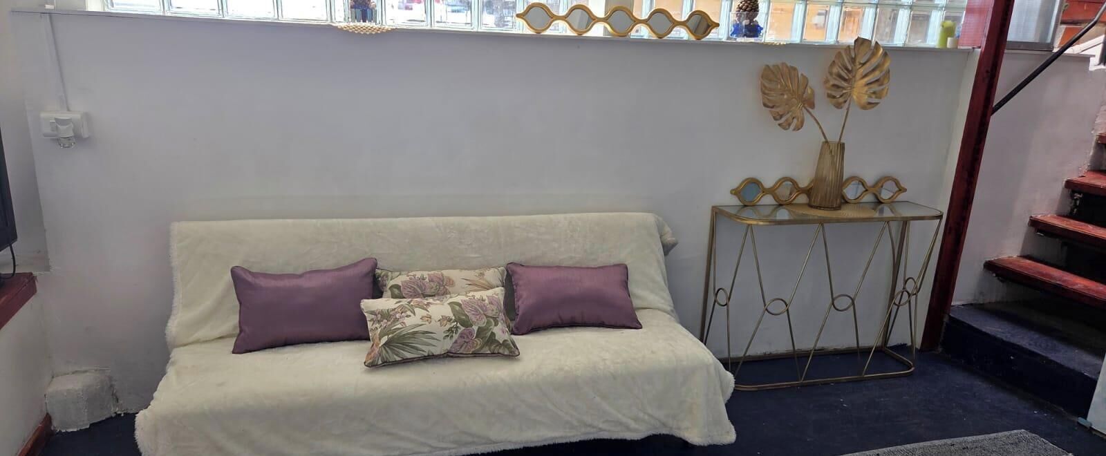 A living room with a sofa, two purple cushions, and a decorative metal table with a vase.