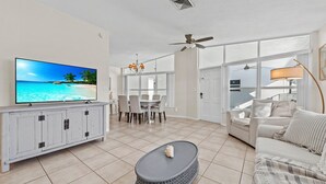 Ein modernes Wohnzimmer mit Flachbildfernseher, einem grauen Couchtisch, einem beige-farbenen Sofa und einem Essbereich mit Tisch und Stühlen.