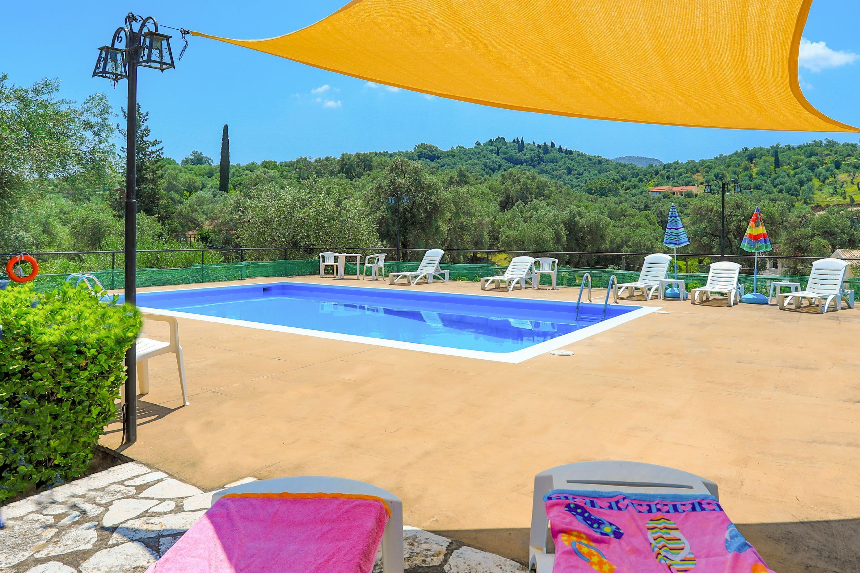 Une piscine entourée de verdure et de collines, avec des chaises longues et des parasols.