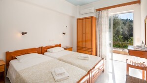 A hotel room with two beds, a wooden wardrobe, a desk with a chair, and a large window offering a view of greenery. - Corfu apartment with shared pool near Saint Spyridon beach (Saint Spyridon)