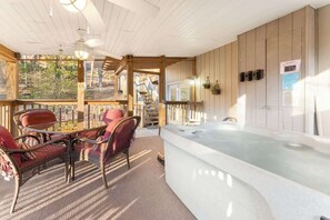 A sunlit outdoor seating area with a hot tub, wooden deck, and a view of a staircase leading to an upper level. - Cozy Mountain Family Getaway with Hot Tub in Prime Location (Pigeon Forge)