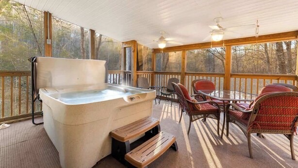 Un espacio al aire libre techado con un jacuzzi, terraza de madera y sillas de mimbre.