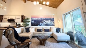 A modern living room with a sofa, a glass coffee table, and a view of a snowy mountain landscape through a large window. - Summit View II | Ski-in · Hot Tub · Sleeps 6 (Kimberley)