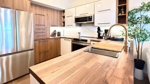 A modern kitchen with stainless steel appliances, wooden cabinets, and a central island with a sink. - Summit View II | Ski-in · Hot Tub · Sleeps 6 (Kimberley)
