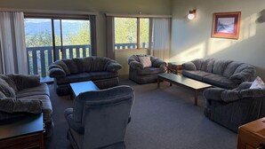 A cozy living room with four grey sofas and a coffee table, large windows with curtains, a wooden ceiling, and a framed picture on the wall. - Summit View II Bed & Bath| Ski-In Hot Tub Sleeps 2 (Kimberley)
