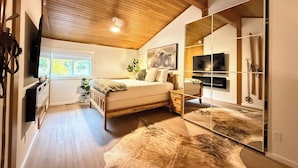 Une chambre avec un plafond en bois, un lit, une télévision, un miroir et un porte-skis.