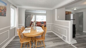 Ein Essbereich mit einem runden Holztisch und Stühlen, einer Vase mit Trockenblumen und einem Bild an der Wand.