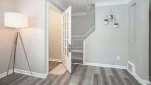 Ein Flur mit Holzboden, einer Lampe, einer Tür zu einer Treppe und zwei hängenden Pflanzen.