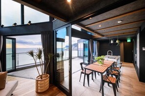 A modern interior with a dining area, large windows, and a view of the sea. - VILLA IZU Zessei (Ito)