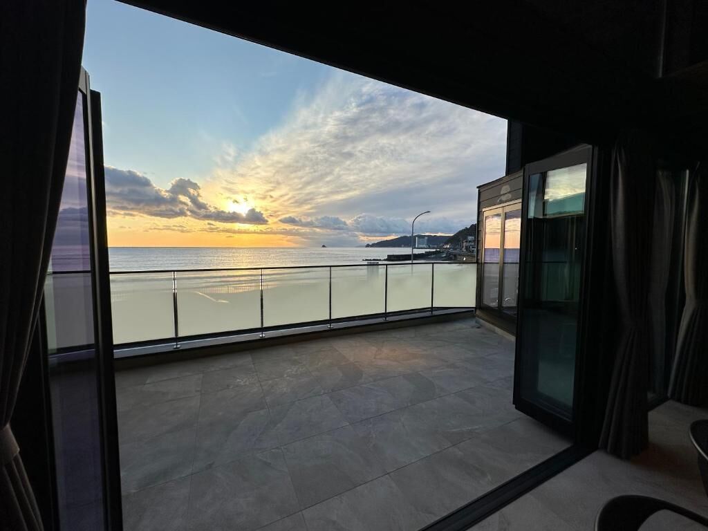 Un balcón con vista al atardecer sobre el agua, una puerta de cristal y una silla.