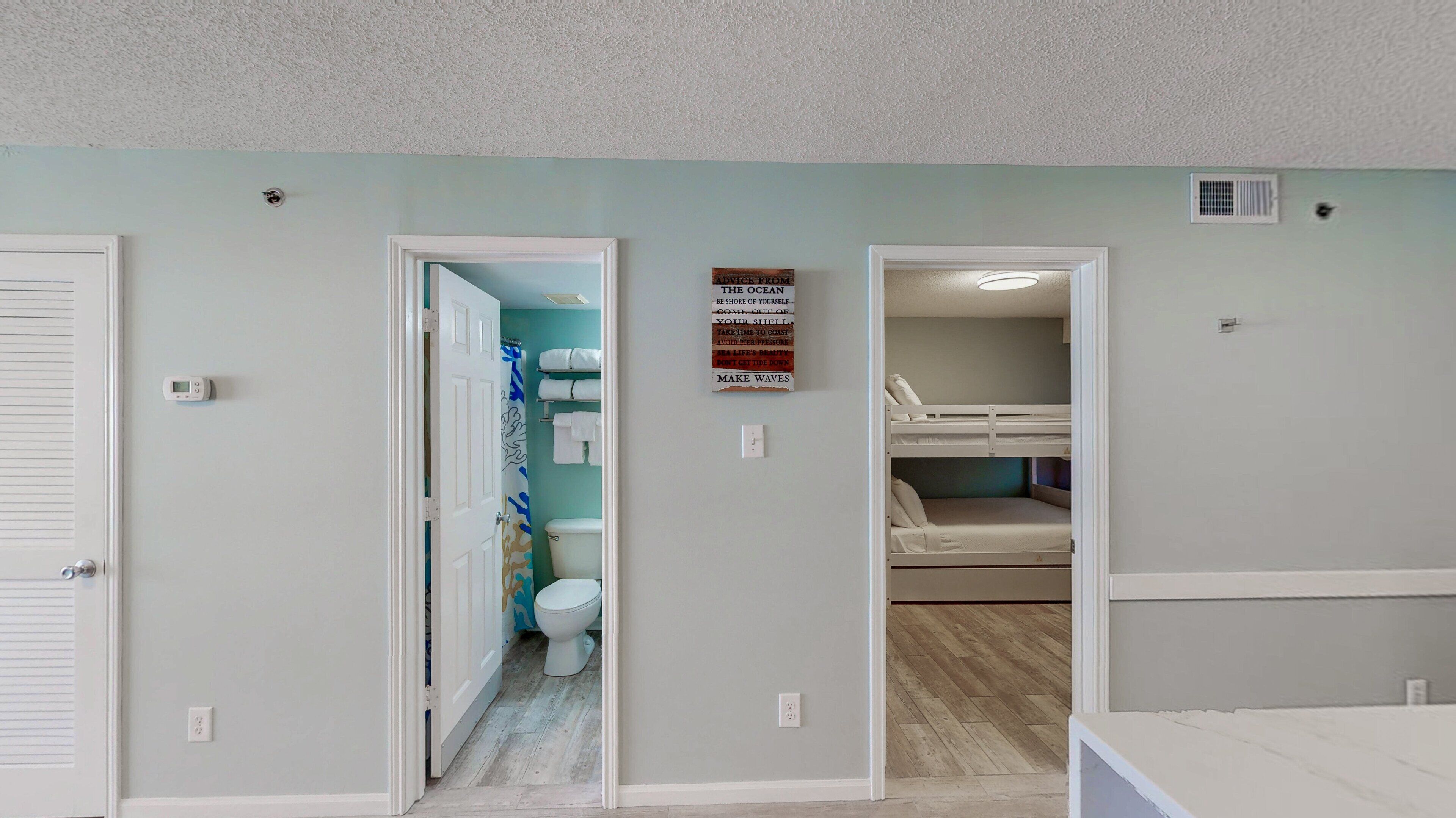 Une pièce avec un lit superposé, des toilettes et une douche. Il y a un panneau sur le mur et un thermostat également fixé au mur.