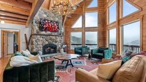 A cozy living room with a stone fireplace, comfortable seating, and large windows offering a view of the outdoors.