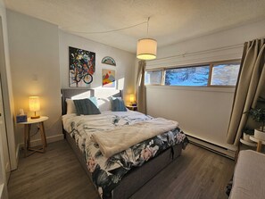 Een slaapkamer met een bed, bedlampjes, een raam met uitzicht op bomen, en kunst aan de muur.