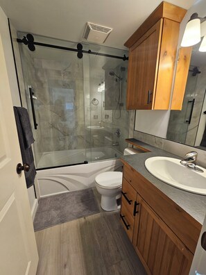 Een moderne badkamer met een douche in een glazen cabine, een badkuip, een wit toilet en houten kastjes.