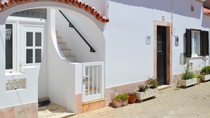 Un edificio blanco con tejado de baldosas, una escalera que conduce a una puerta y plantas en macetas en el suelo.