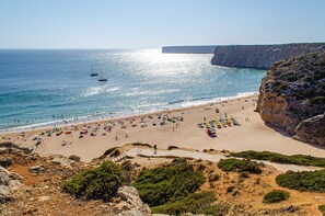A beach with a rocky cliff, a clear sky, and a calm sea. - Casa Vitorino – 5 minutes’ walk from Mareta Beach. (Sagres)