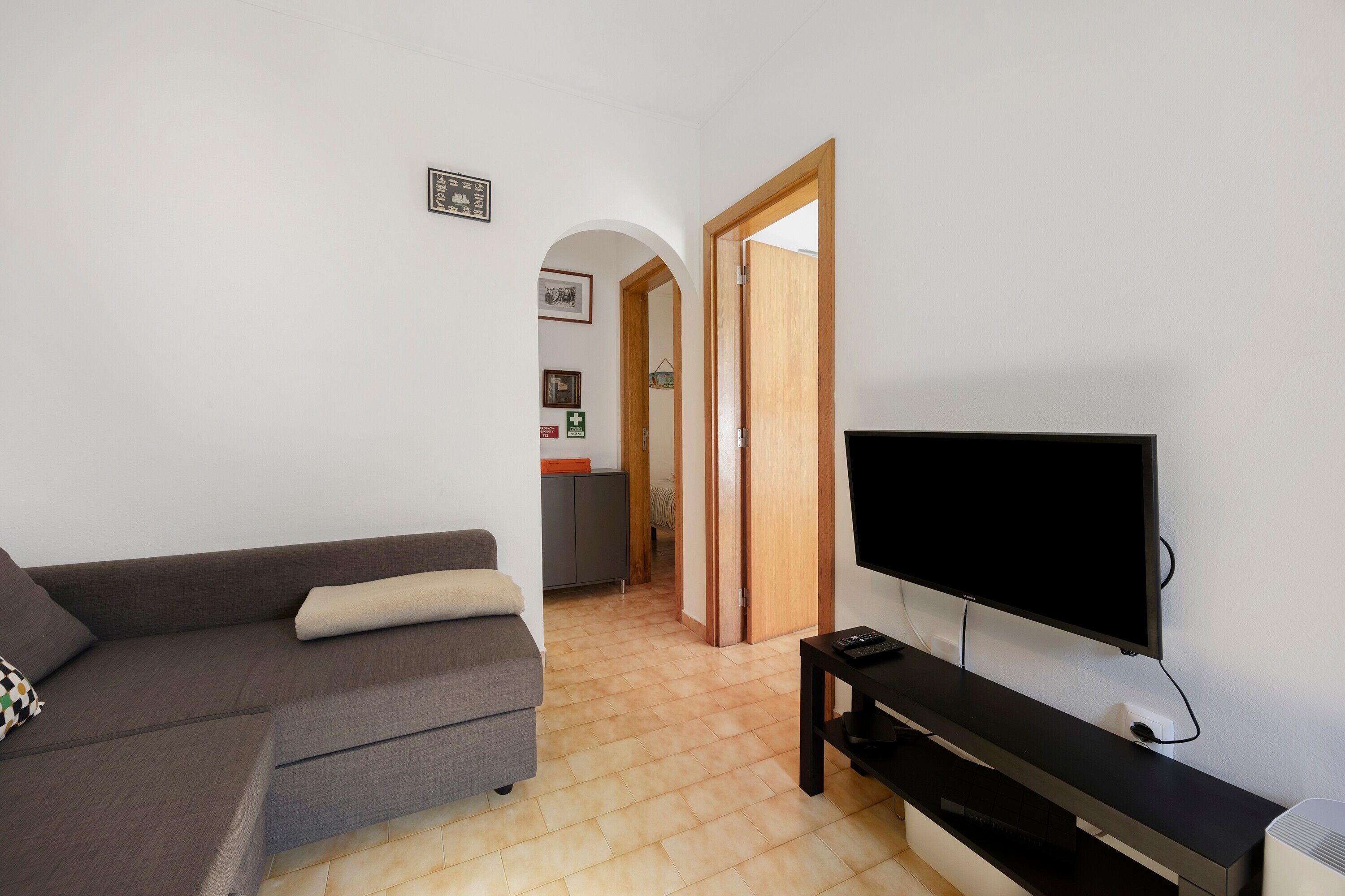 Un salon comprenant un canapé, un téléviseur à écran plat et une porte en bois donnant sur une autre pièce.