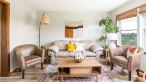 Ein Wohnzimmer mit einem beigen Sofa, zwei Sesseln, einem Holztisch und einem gemusterten Teppich.