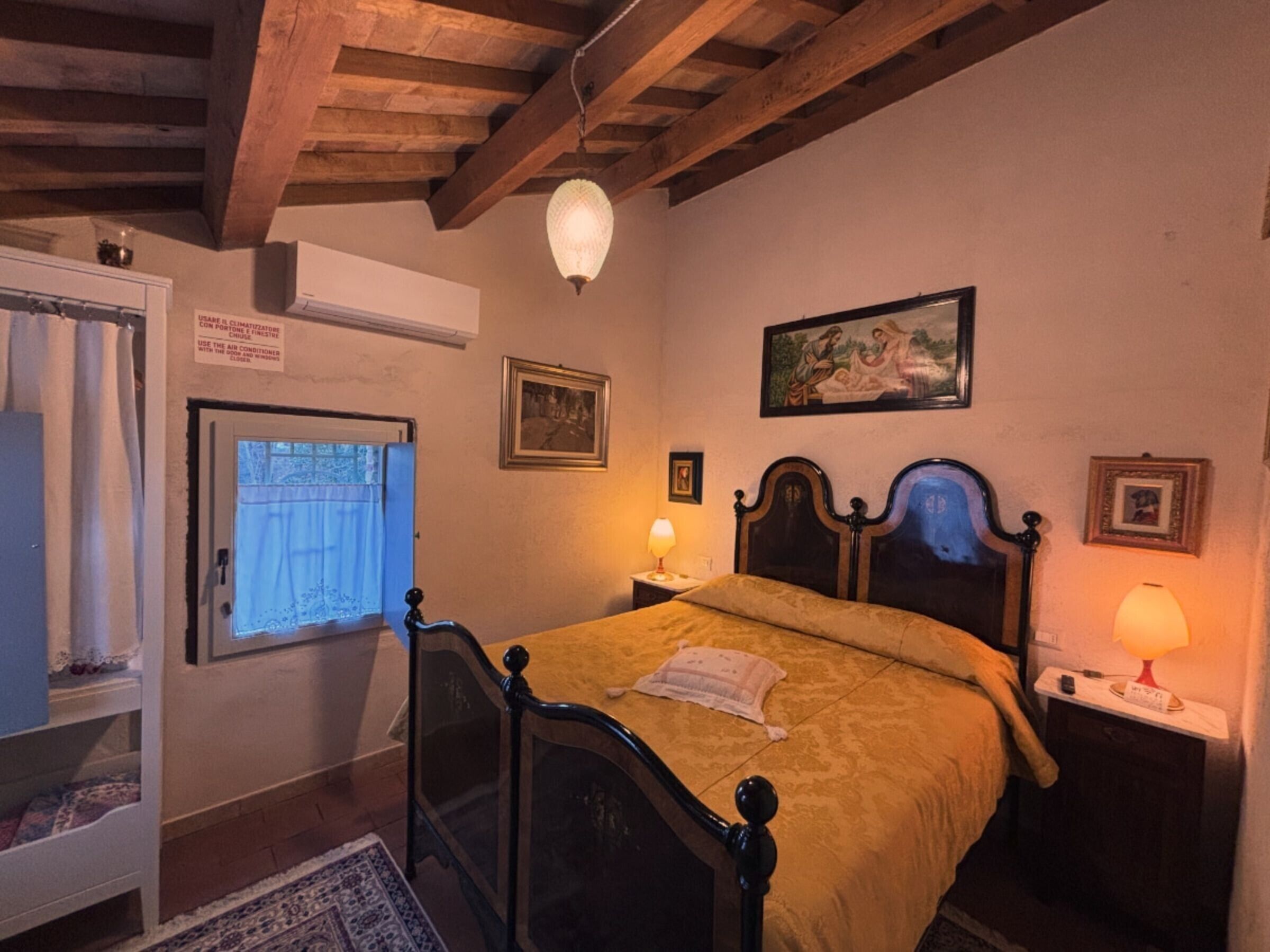 Ein Schlafzimmer mit einem hölzernen Bett, einem Nachttisch mit Lampe, einem Fenster mit Vorhängen und einem Bild an der Wand.