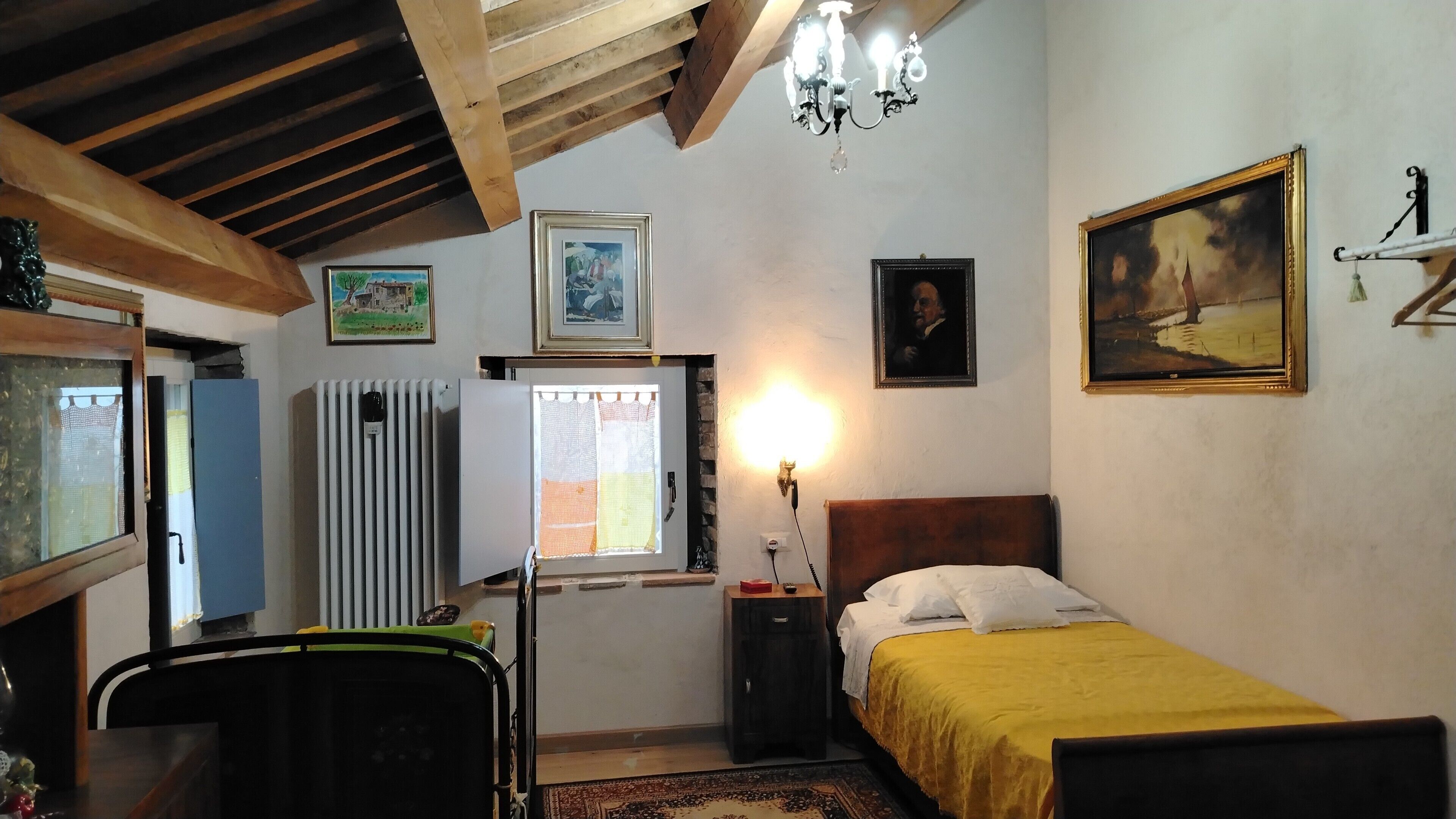 Une chambre à coucher avec un lit, un radiateur, une fenêtre avec des rideaux, un lustre et des tableaux encadrés accrochés au mur.