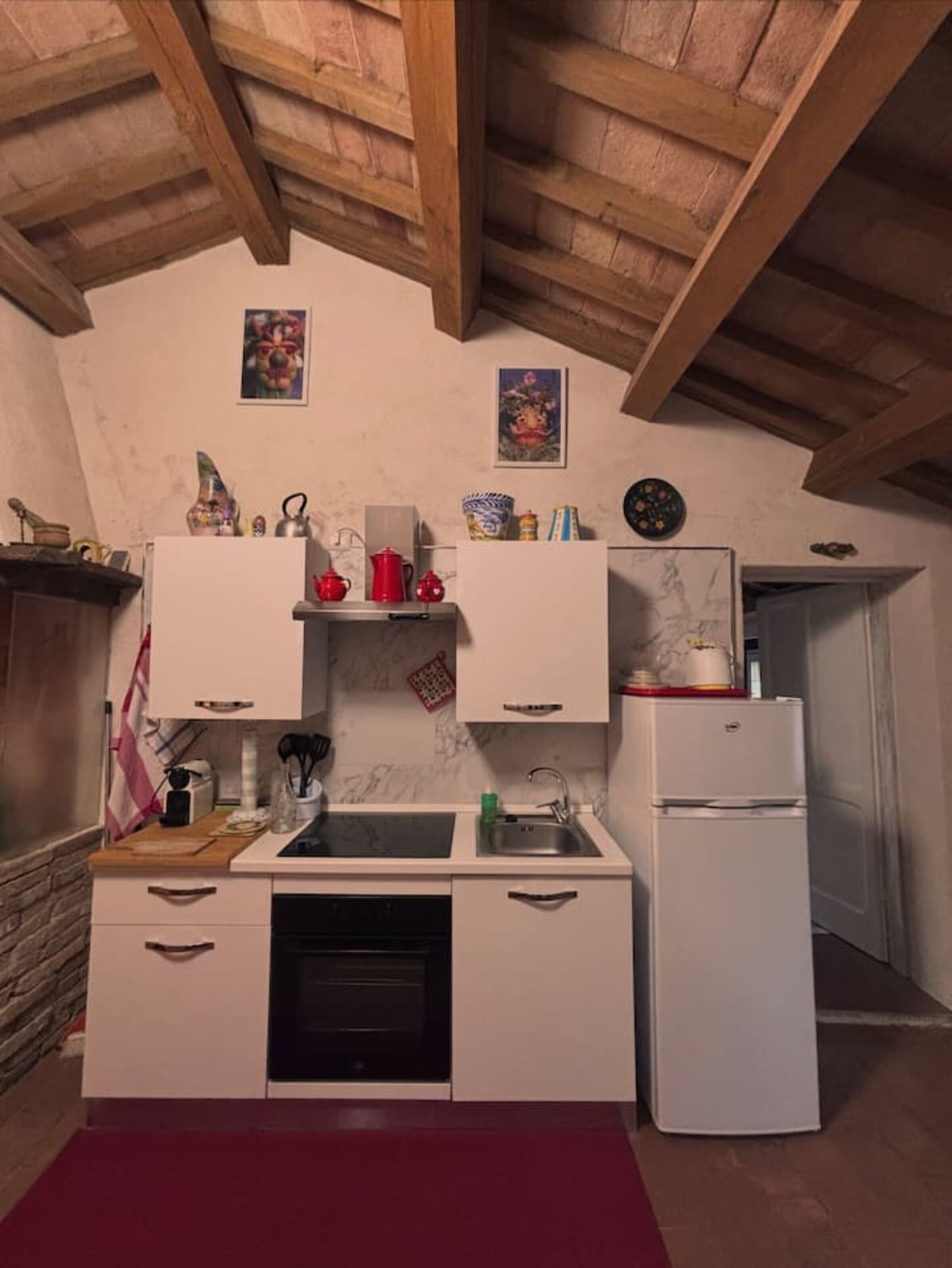 A compact kitchen with a built-in oven, a sink, and a white refrigerator. There are decorative items on the countertop and a clock on the wall.