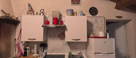 A compact kitchen with a built-in oven, a sink, and a white refrigerator. There are decorative items on the countertop and a clock on the wall.