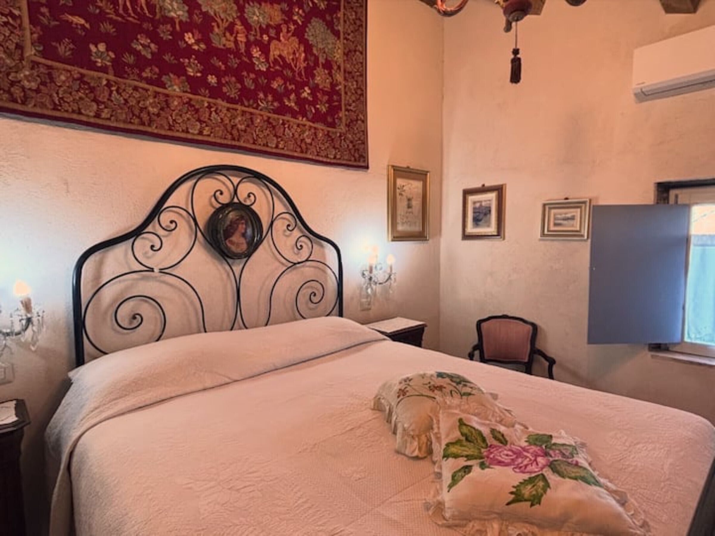 Een slaapkamer met een bed, een stoel, een televisie en een muur met foto’s.