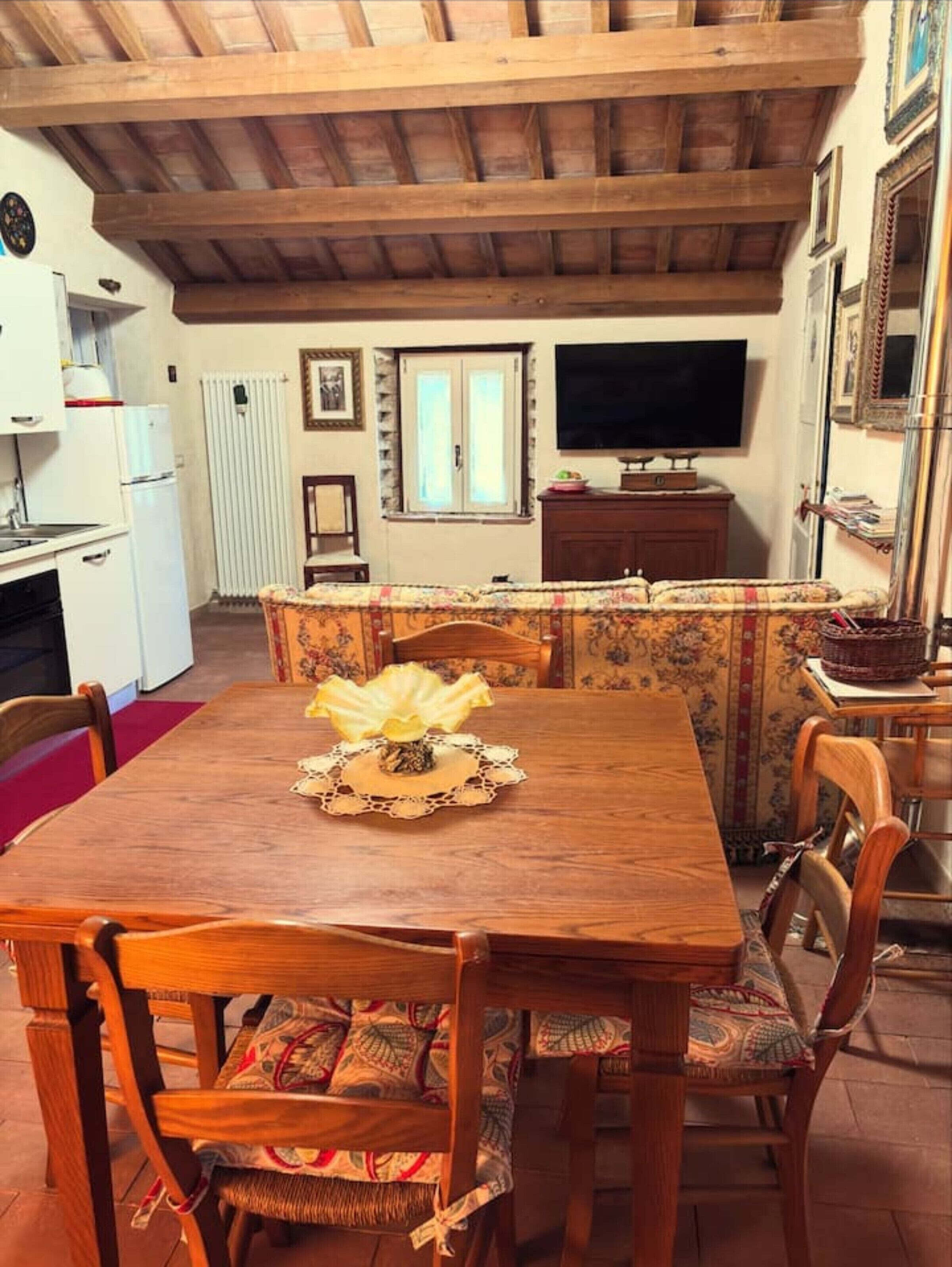 A dining area with a wooden table, chairs, a television, and a kitchen area with a refrigerator and stove.