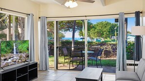 A living room with a TV, sofa, and a table. There is a sliding glass door leading to an outdoor patio with chairs and a table. - Ground floor, updated studio, across from the beach! - Kihei Bay Surf A101 (Kihei)