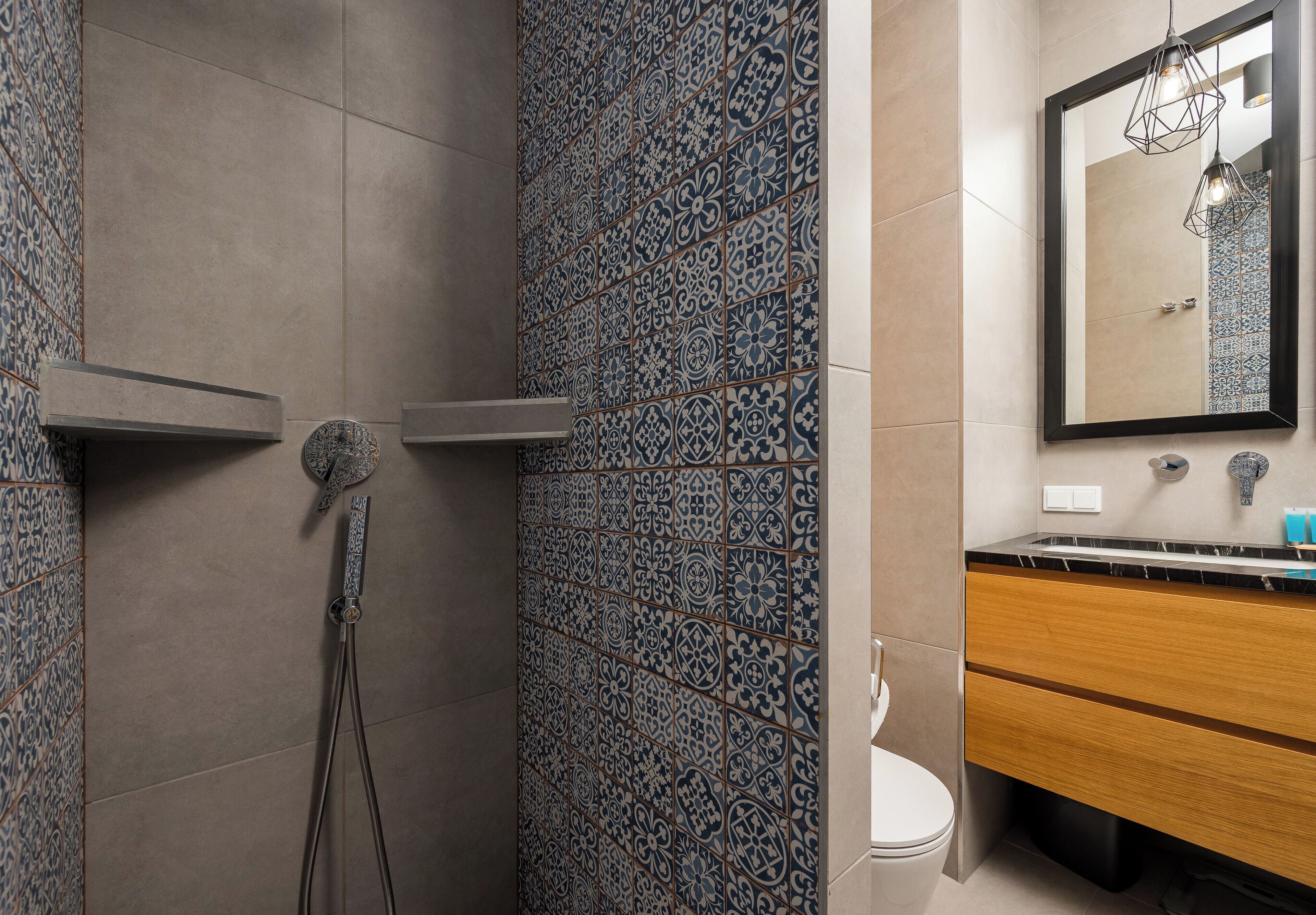 A bathroom with patterned tiles, a shower, a toilet, a vanity with a mirror, and a hanging light fixture.